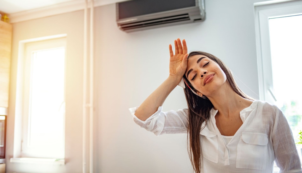 Woman in white shirt raising hand indoors near window and AC unit. AC Not Blowing Cold Air.